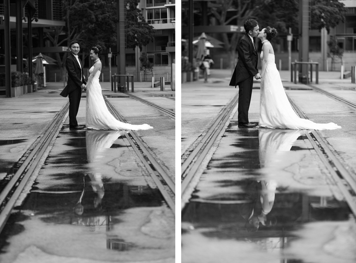 Black and white dual shot of the bride and groom standing on the old train tracks at the Rocks in Sydney holding hands and kissing while they are reflected in puddles on the ground Sydney wedding photographer