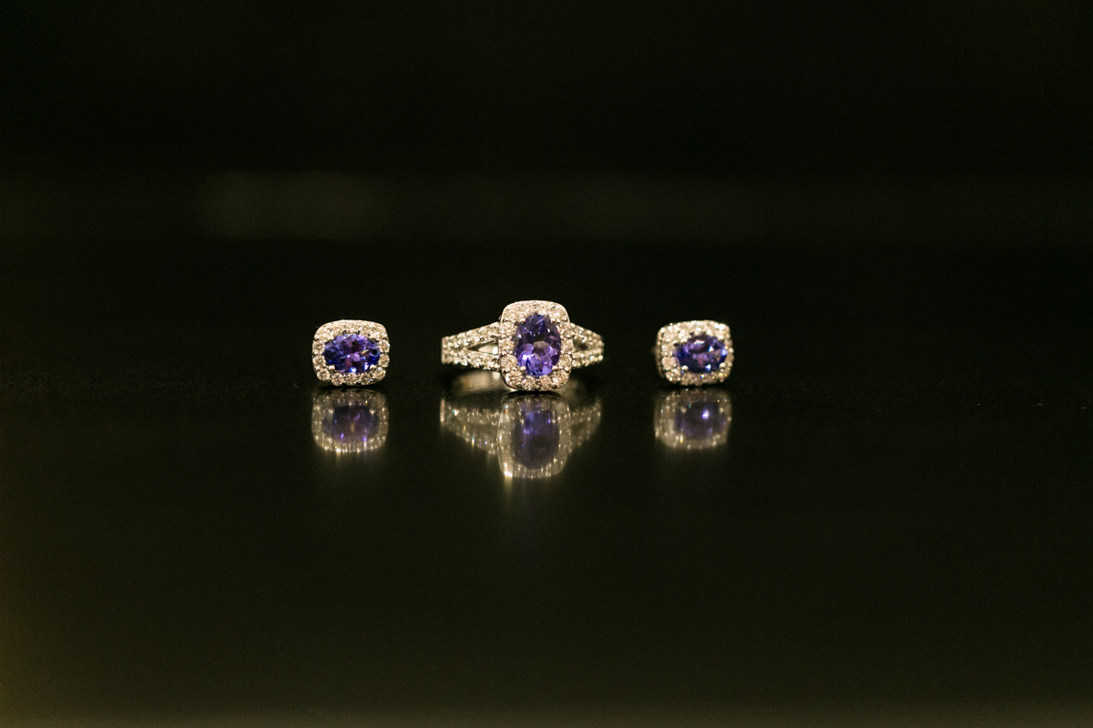 Close up shot of gold ring and earrings with purple gemstones in a reflective tabletop on a black background Caves Beach wedding photography