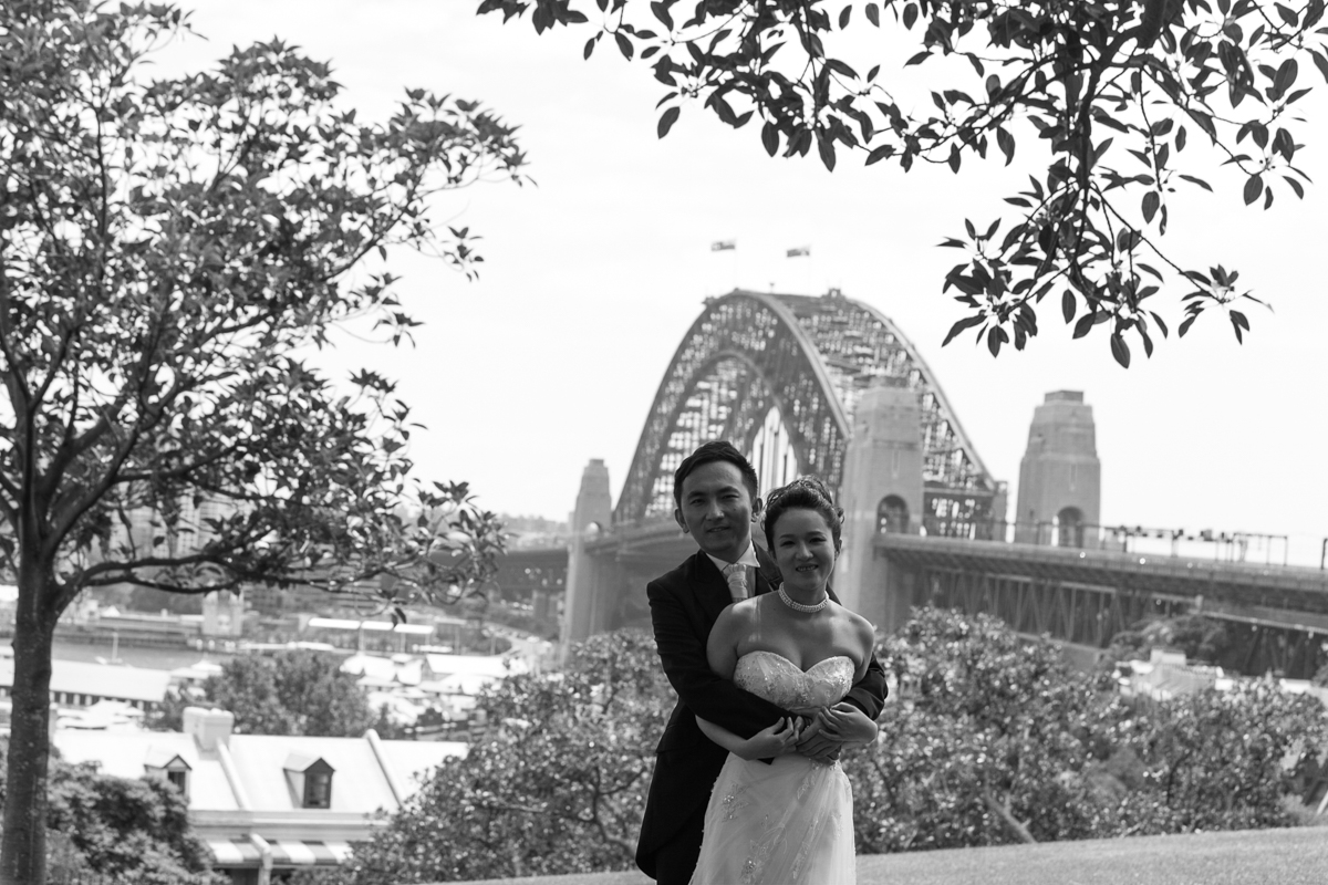 Black and white shot of the bride and groom embracing facing the camera with the Sydney Harbour Bridge in the background Sydney wedding photographer