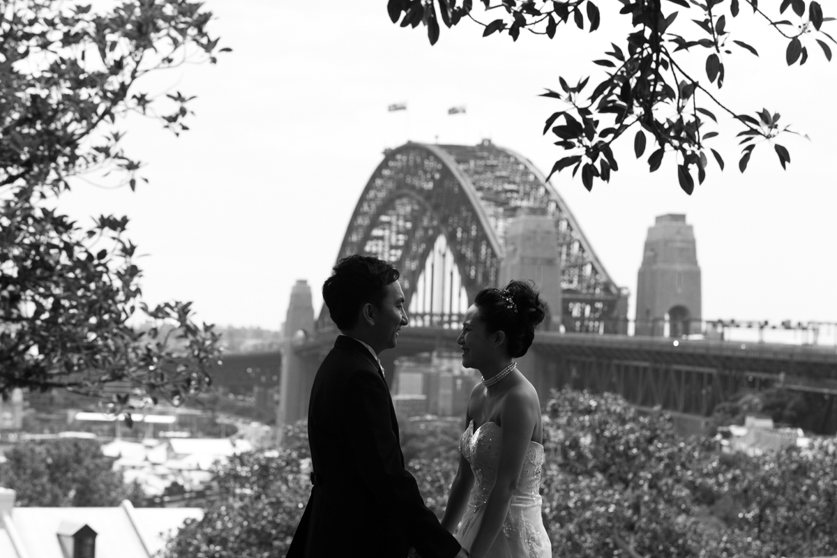 Black and white landscape shot of the bride and groom holding hands with the Sydney Harbour Bridge in the background Sydney wedding photographer