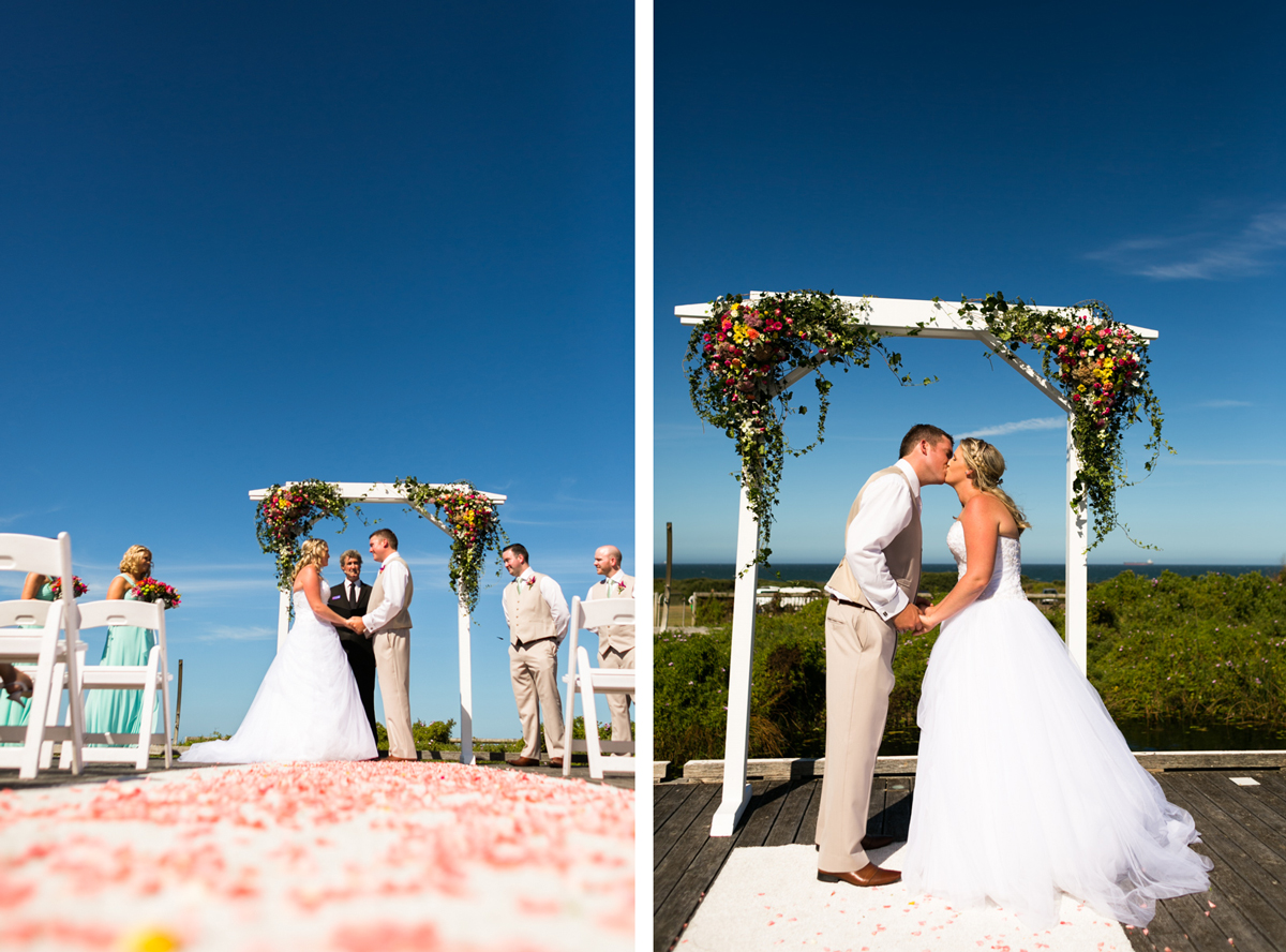 Dual shot of the bride and groom at the altar holding hands, and kissing under the white wooden arch with an expanse of blue background behind them and pink rose petals on the white aisle runner Caves Beach wedding photography