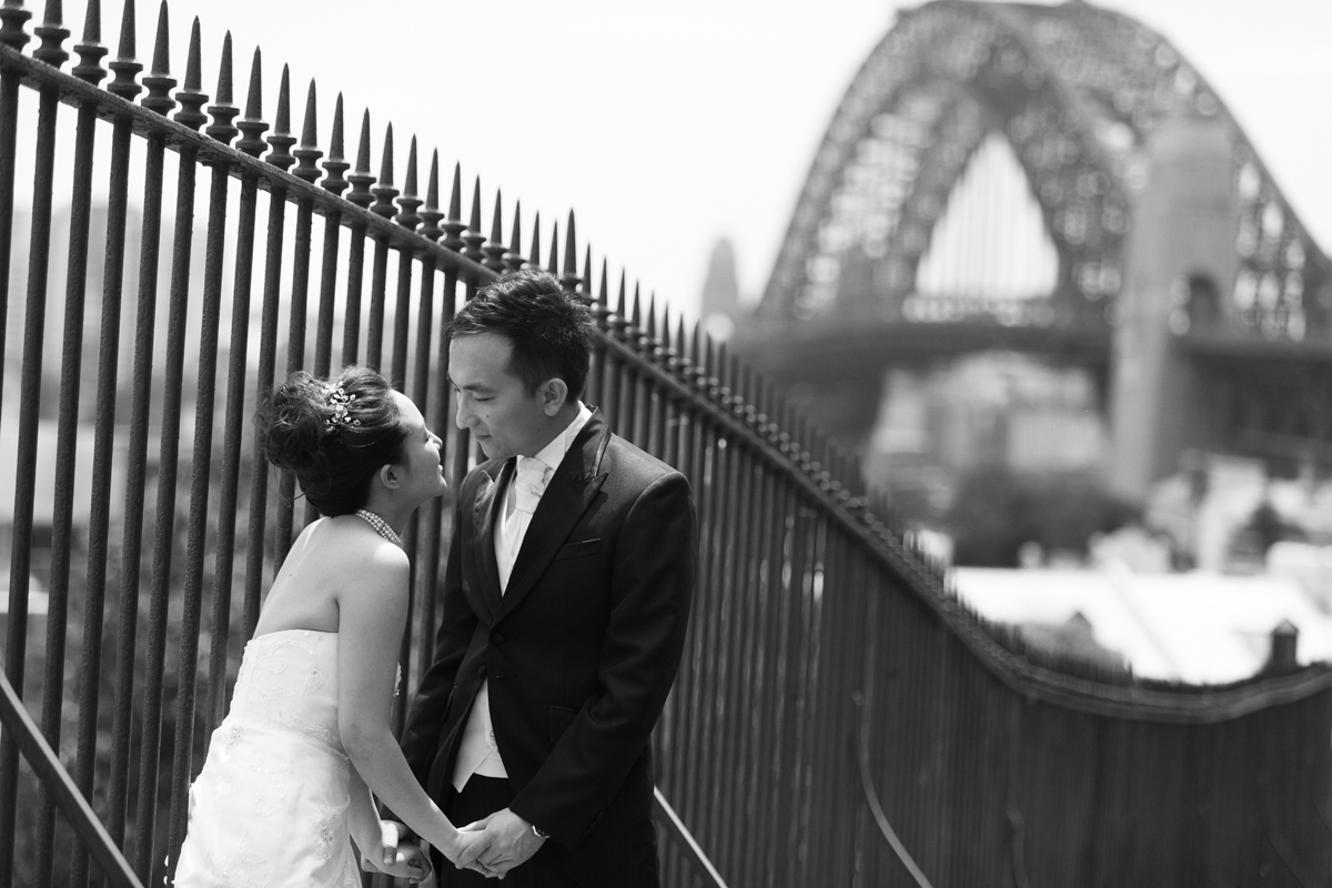 Candid shot of the bride and groom looking into each others eyes standing next to a black iron fence with the Sydney Harbour Bridge in the background Sydney wedding photographer