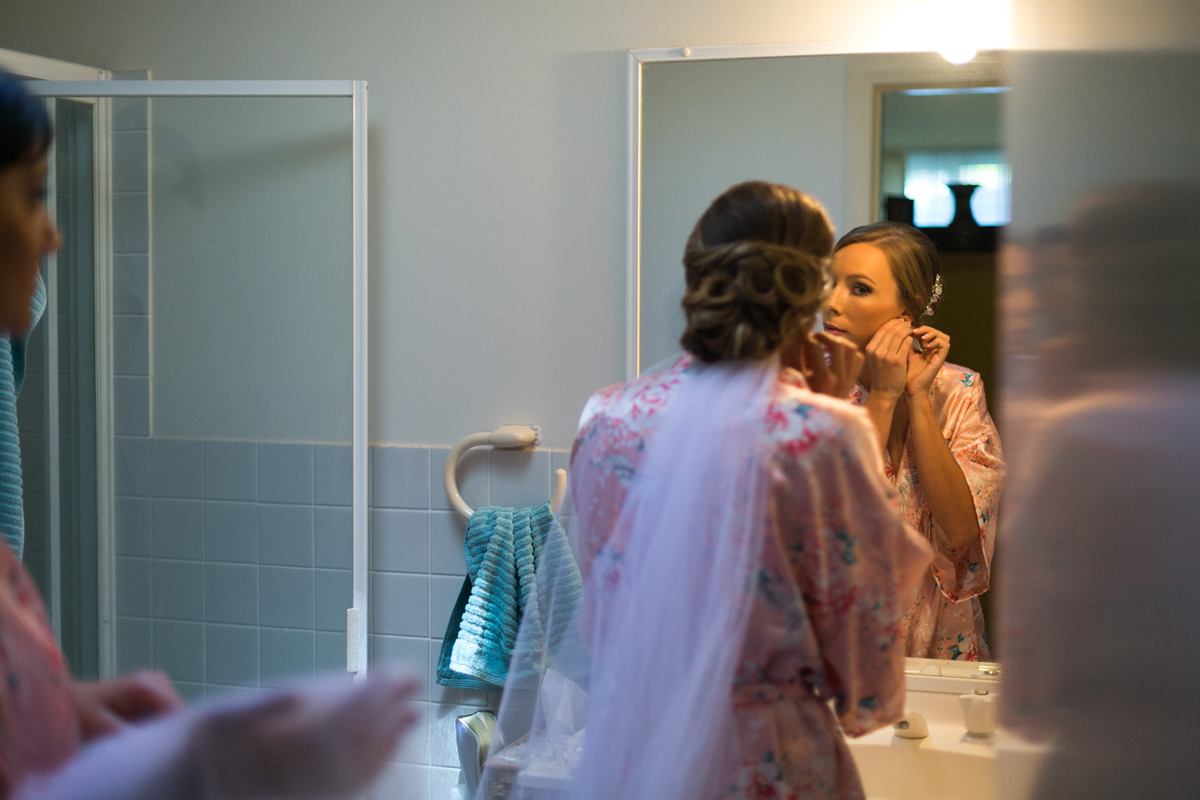 Candid shot of the bride putting her earrings in wearing a pink kimono and her veil Tocal Homestead wedding photographer