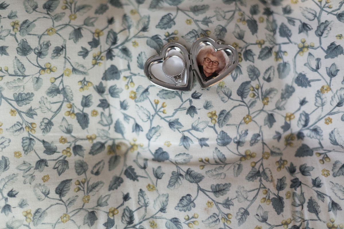 Close up of a silver heart locket open showing a photo of grandmother and the bride's engagement ring on a blue floral tablecloth Tocal Homestead wedding photographer