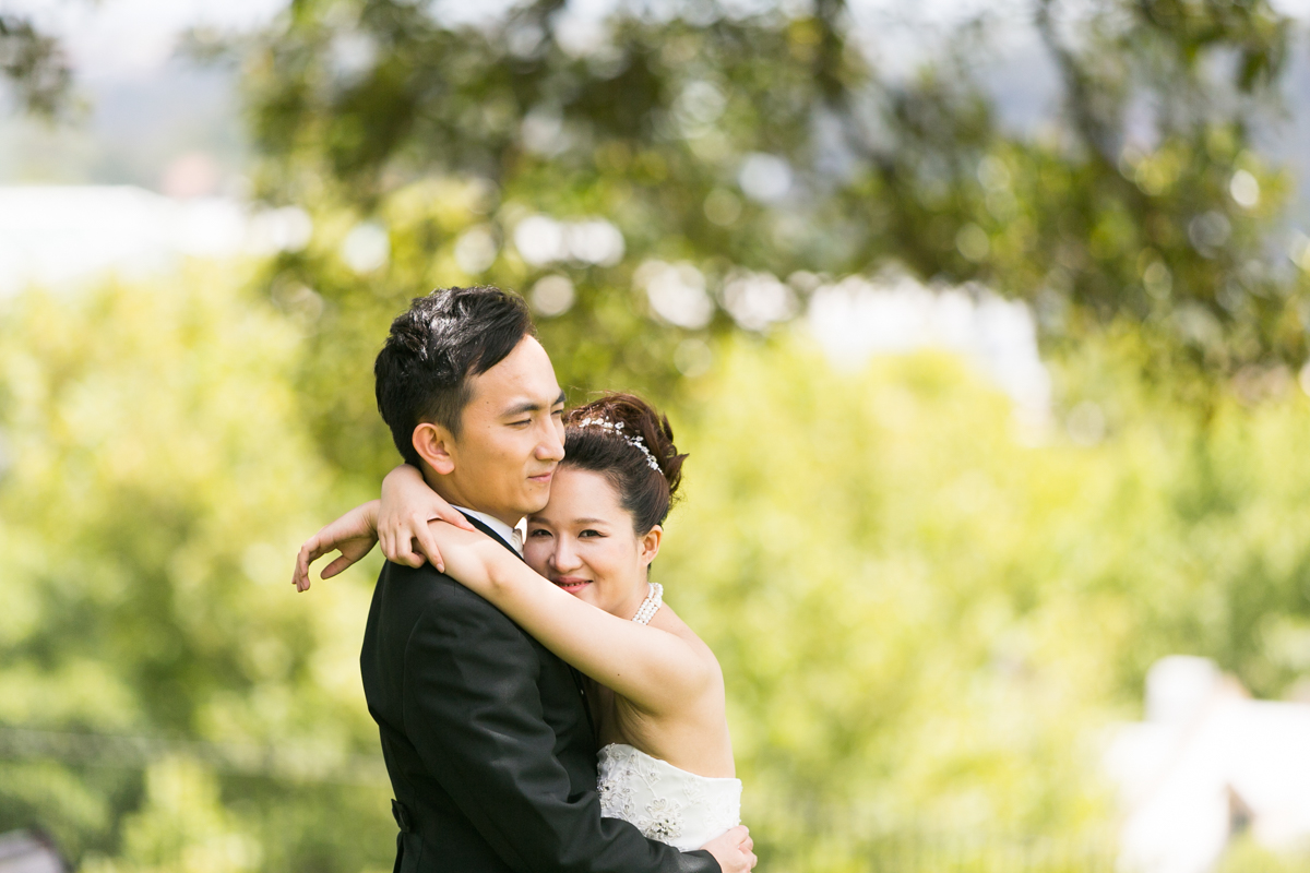 The bride and groom standing with their arms around each other with unfocused greenery in the background Sydney wedding photographer