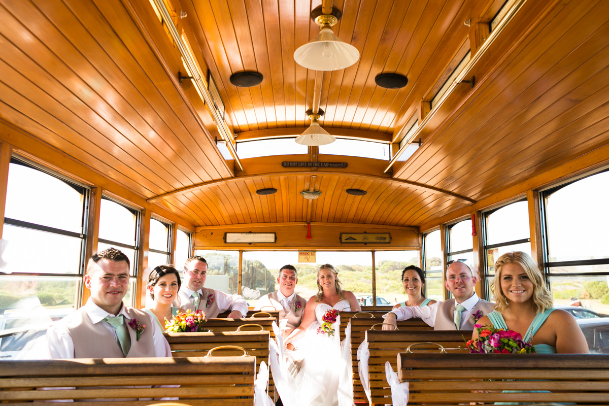 The bride and groom sit on Newcastle's Famous Tram with their bridal party Caves Beach wedding photography
