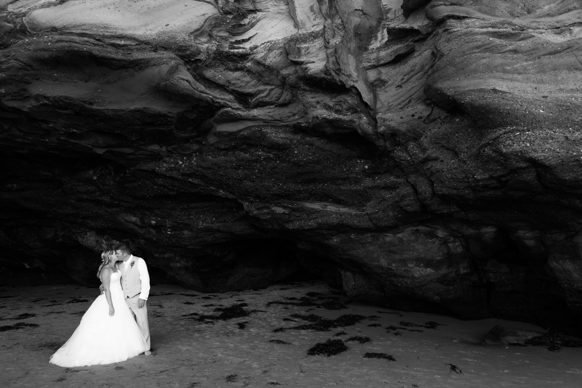 Black and white shot of the bride and groom kissing standing in a natural beach cave Caves Beach wedding photography