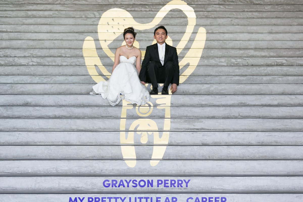 Artistic shot of the bride and groom sitting on cement steps decorated with a gold painted figure by Grayson Perry at the Museum of Contemporary Art Sydney wedding photographer