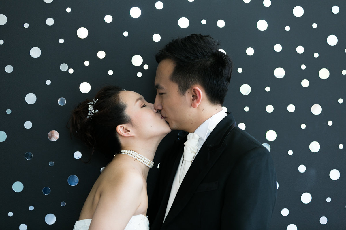 The bride and groom kiss in front of a black wall covered in small round mirrors at the Museum of Contemporary Art Sydney wedding photographer