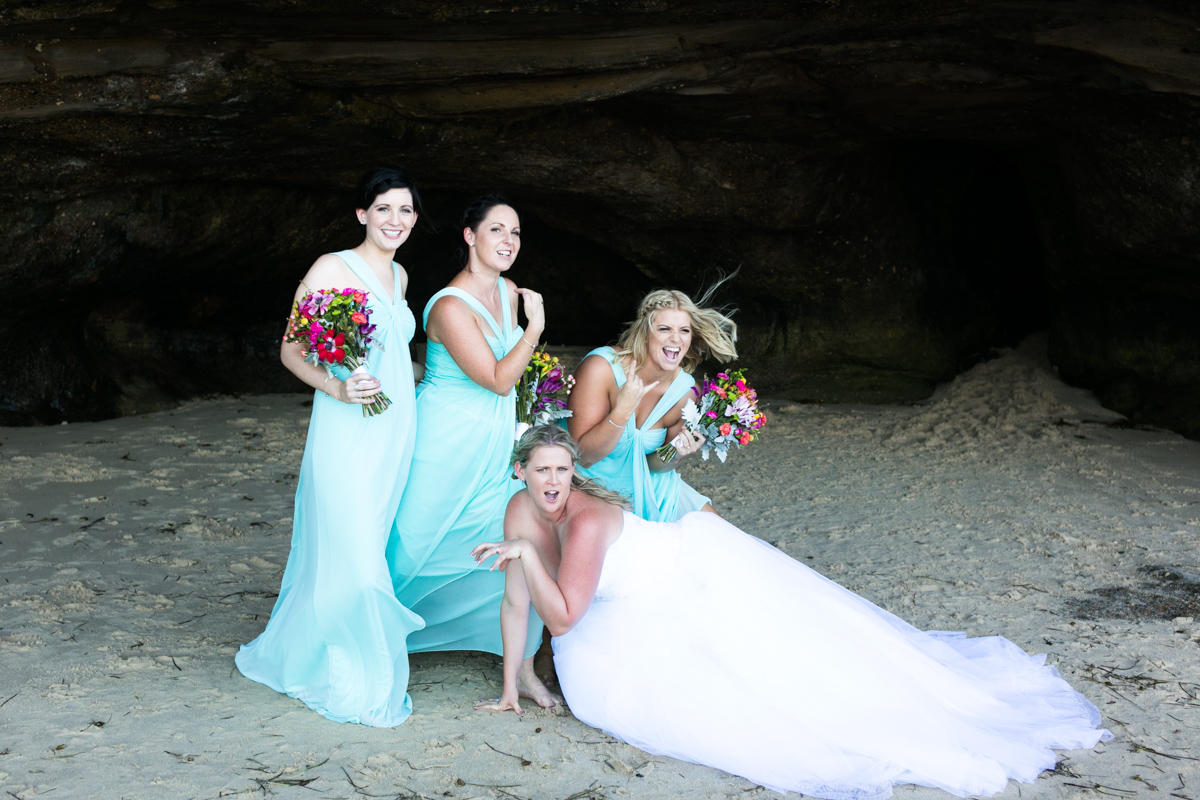 Candid shot of the bride and bridesmaids pulling silly faces and poses in the mouth of a natural beach cave Caves Beach wedding photography