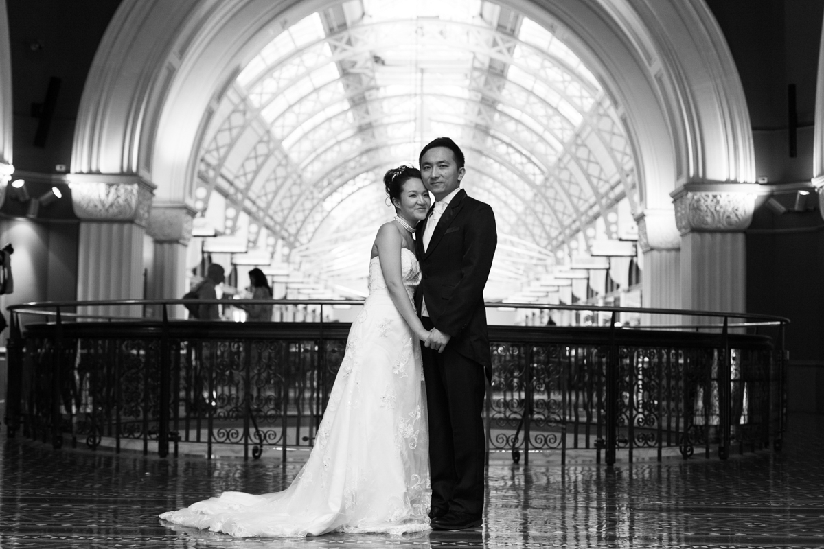 Black and white shot of the bride and groom standing together in the centre of the top floor of the Queen Victoria Building with the arched ceilings and the wrought iron railings behind Sydney wedding photographer