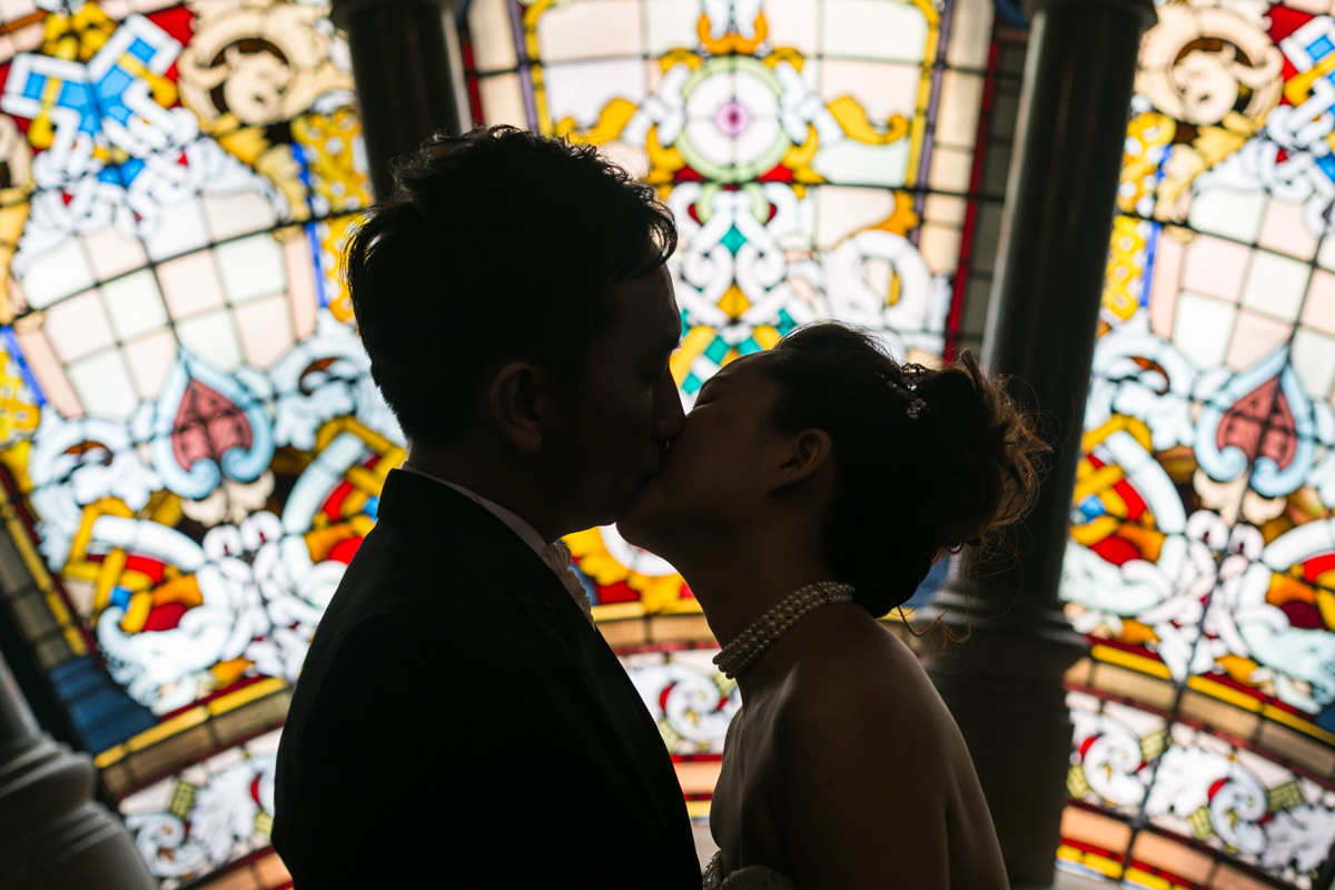 The bride and groom kiss silhouetted against the stained glass windows of the Queen Victoria Building Sydney wedding photographer