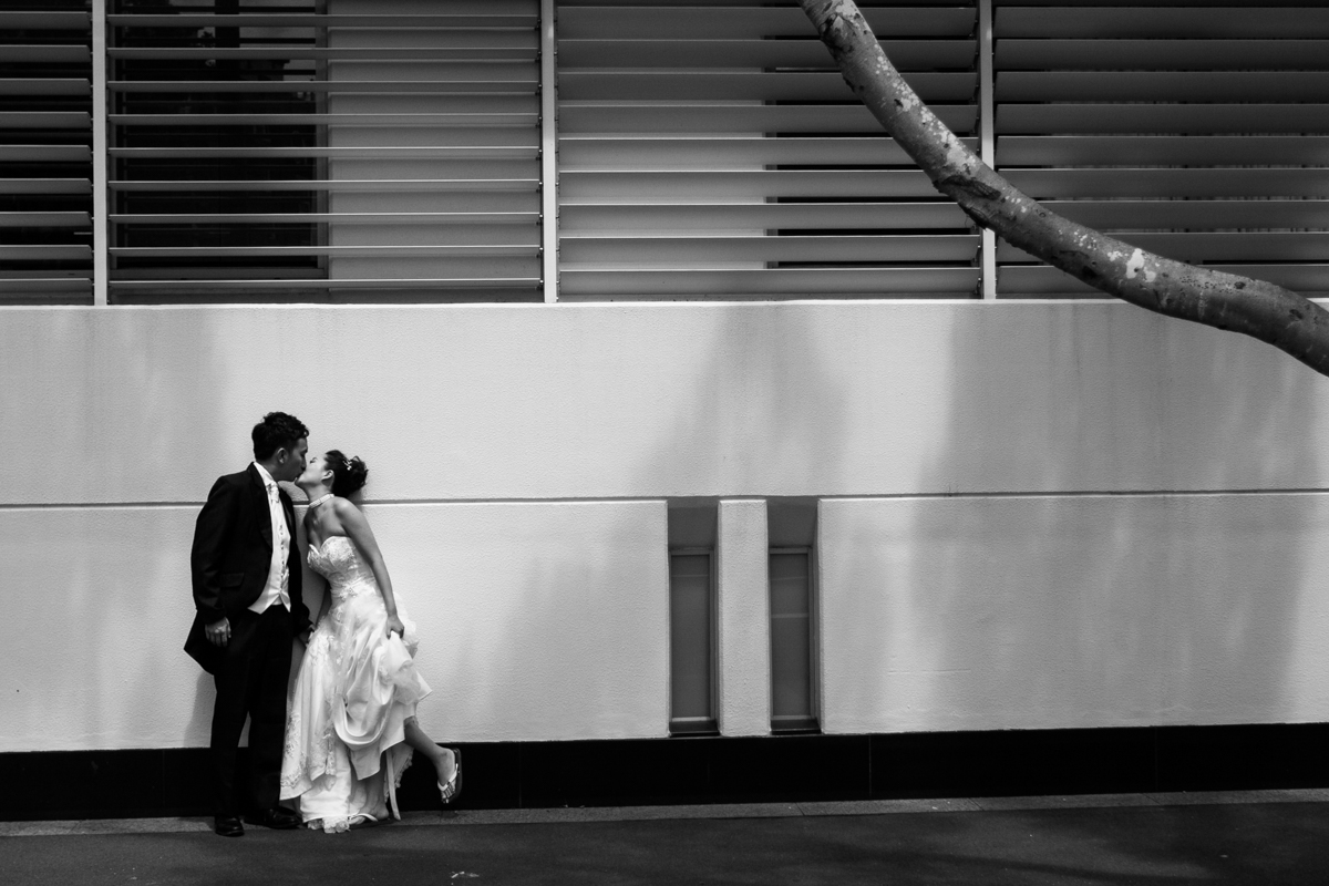 Black and white shot of the bride and groom kissing in front of an industrial commercial building wall Sydney wedding photographer