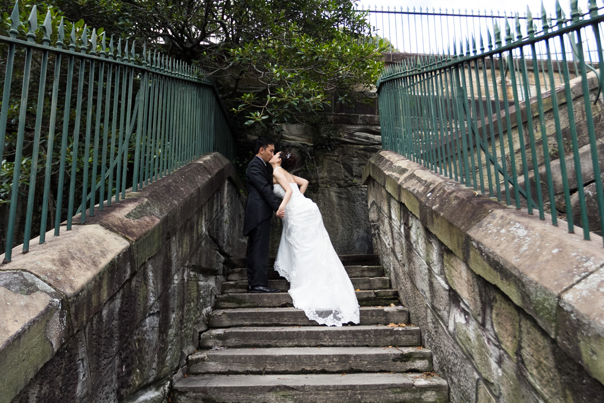 Shot of the bride and groom kissing looking up a set of old stone stairs surrounded by green iron fence Sydney wedding photographer