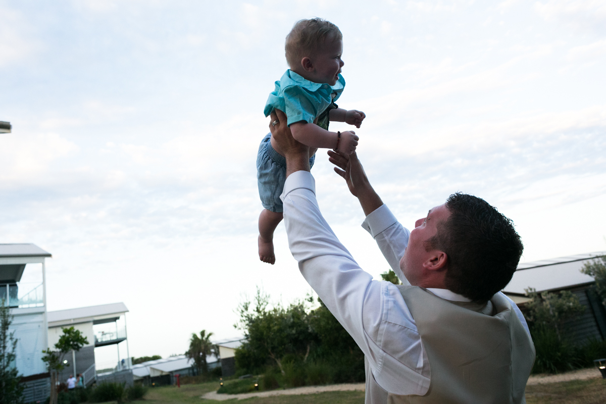 Candid shot of the groom tossing his young son into the air Caves Beach wedding photography