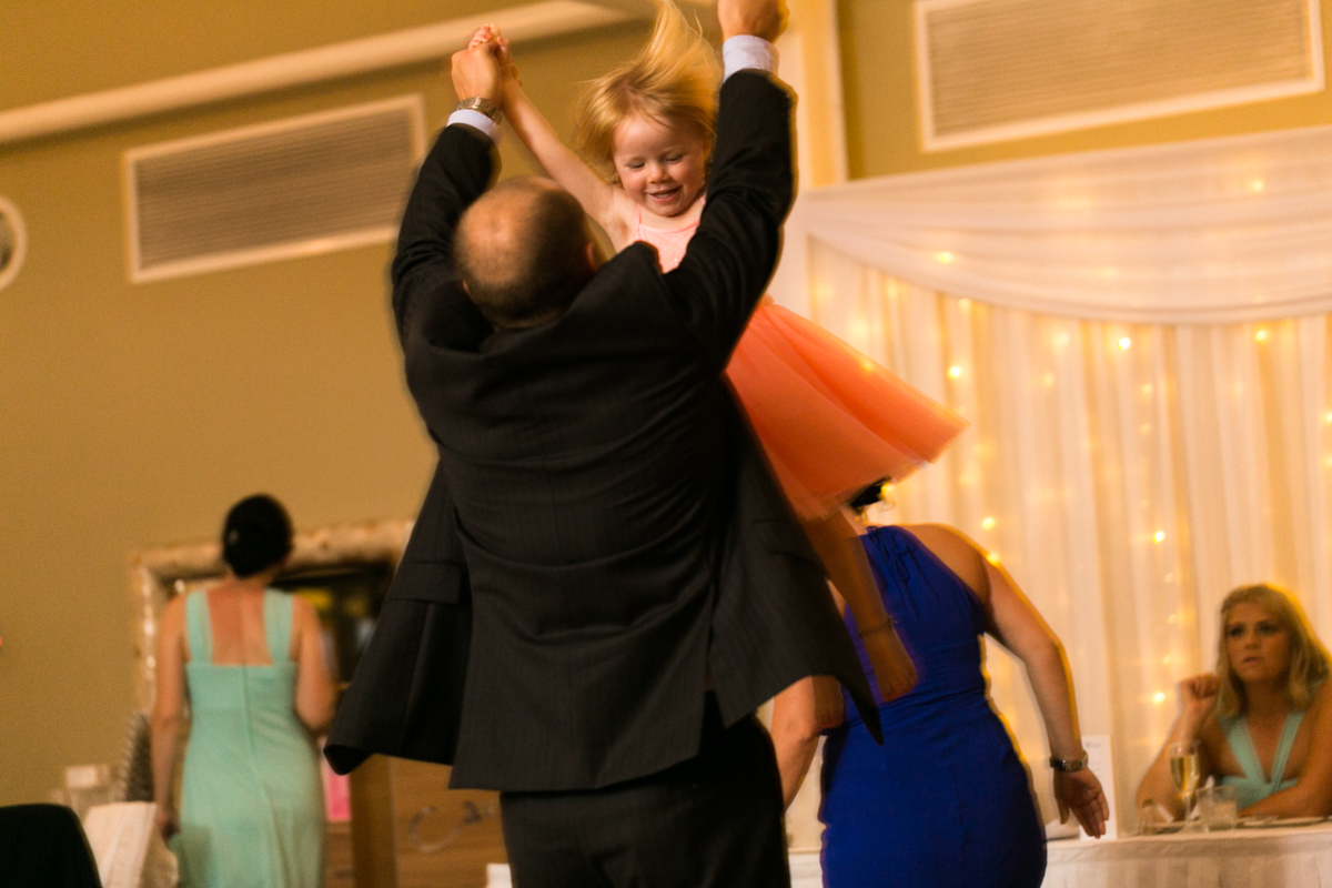 Candid action shot of a wedding guest lifting a small girl into the air and spinning her around on the dance floor Caves Beach wedding photography